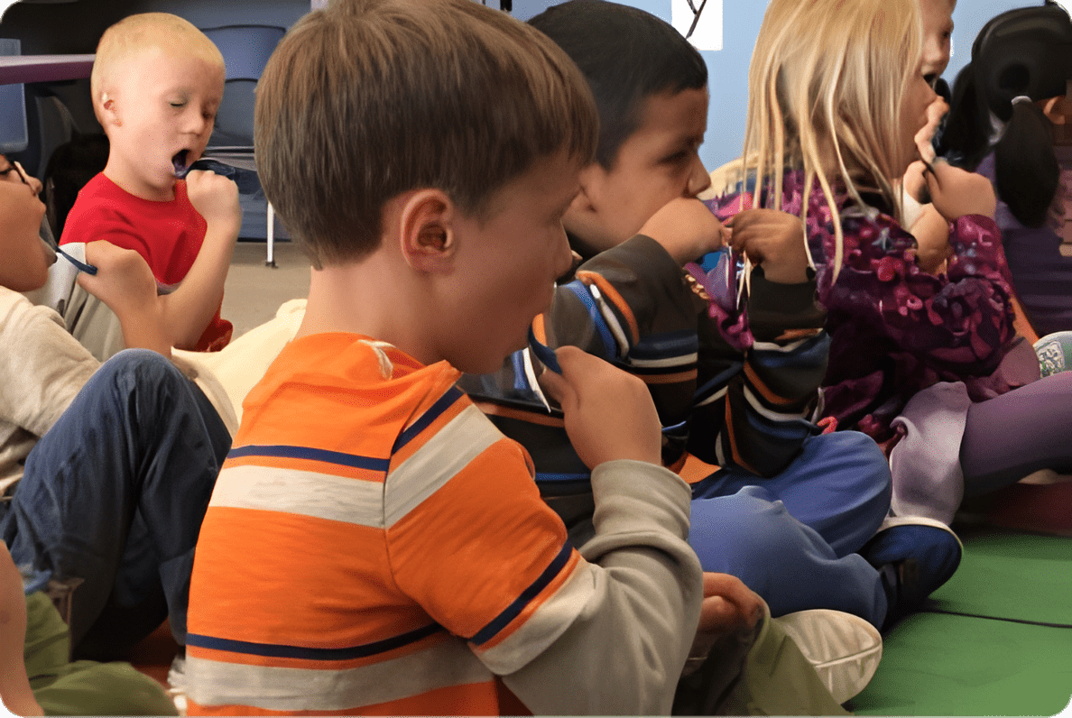 A group of children sitting in the floor eating.