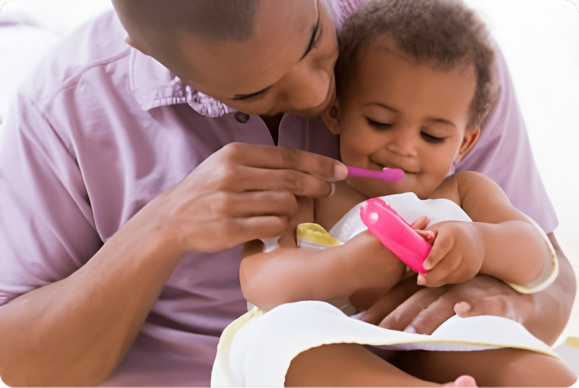 A man is holding a baby and brushing their teeth