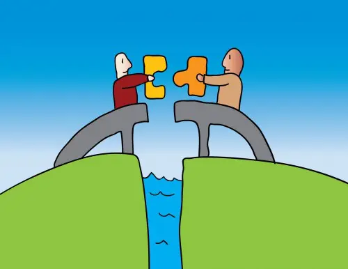 Two people are holding hands and connecting puzzle pieces.