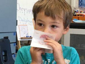 A young boy holding up an envelope with his mouth.