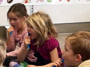 A group of children sitting on the floor brushing their teeth.