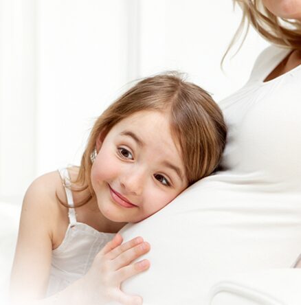 A little girl sitting on the arm of her mother.