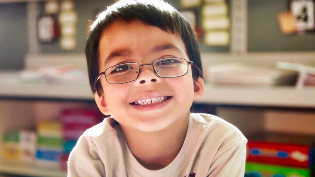 A young boy with glasses smiling for the camera.