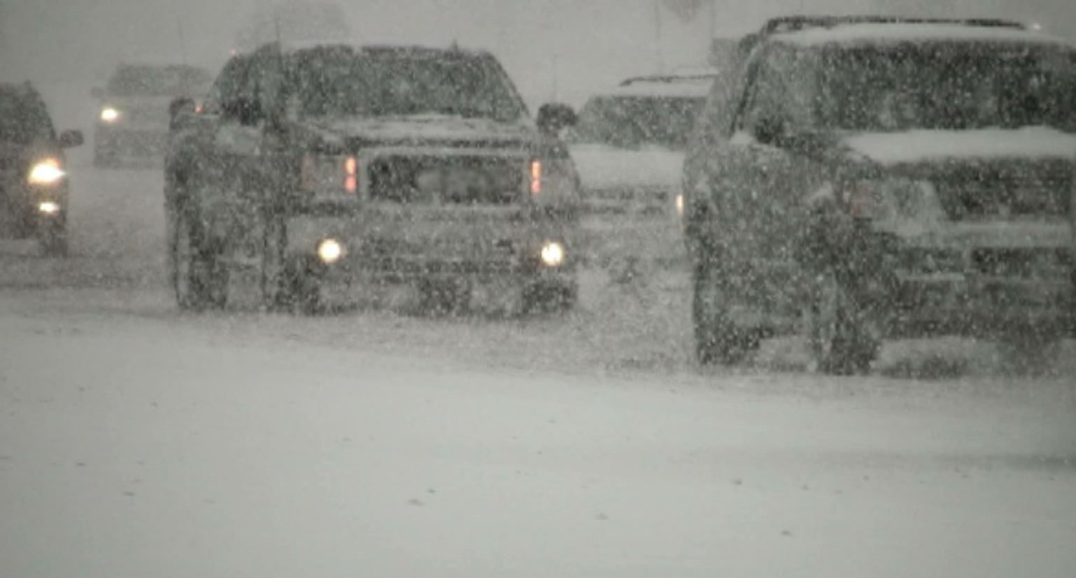 A snowy day with cars driving in the snow.