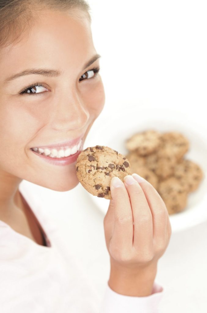 A woman holding a cookie while eating it.