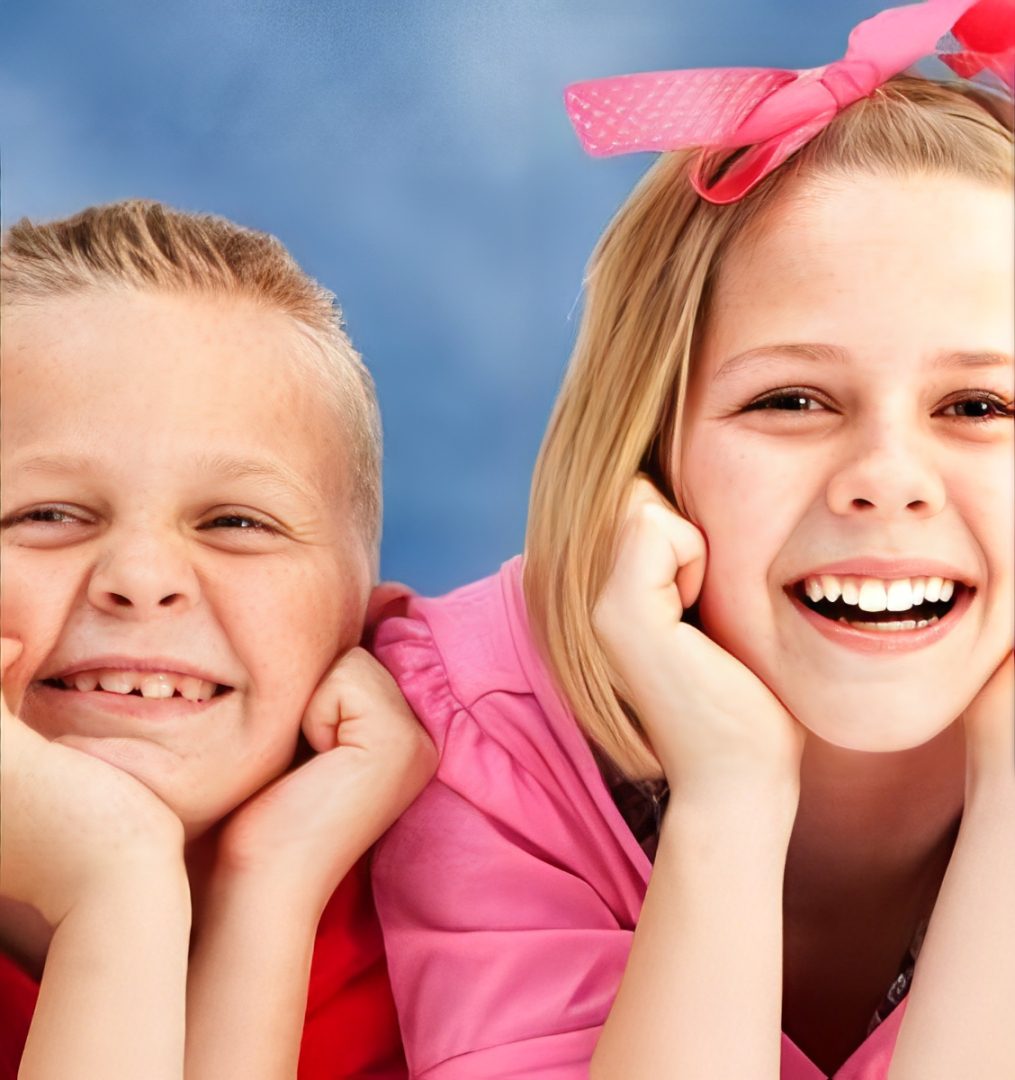 Two children smiling for the camera with their hands on their chests.